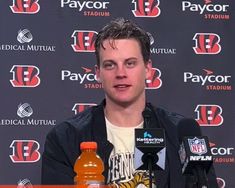 a man sitting in front of microphones at a press conference with two bottles of orange juice