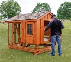 a man standing next to a wooden chicken coop in the middle of a grass field