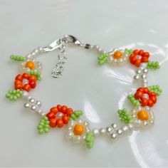 an orange, green and white beaded bracelet on a white surface with silver beads