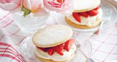 strawberry shortcakes with whipped cream and strawberries on a glass plate next to pink roses