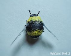 a yellow and black insect with two antennae on it's back legs, sitting on a white surface