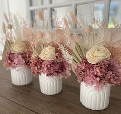 three white vases filled with flowers on top of a wooden table