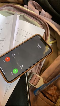 a cell phone sitting on top of an open book in front of a backpack filled with papers