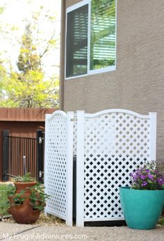 two potted plants sitting next to a white fence in front of a house with brown walls