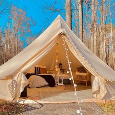 a tent set up in the middle of a forest with two beds and tables inside