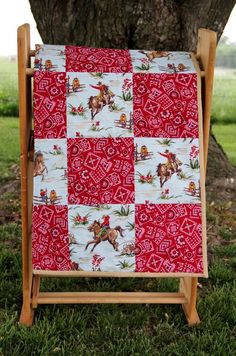 a red and white patchwork quilt on a wooden stand in front of a tree