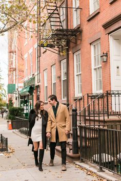 a man and woman are walking down the sidewalk in front of some brick buildings on a fall day