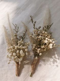 two carrots with flowers are laying on a white sheet and one has long, thin stems