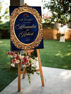 a sign with flowers on it in front of some grass and trees at a wedding