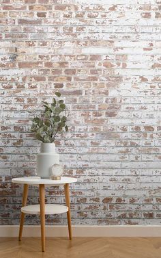 a white table with a potted plant on it in front of a brick wall