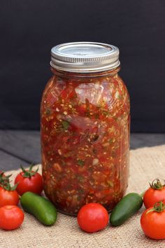 a jar filled with tomatoes and peppers on top of a table next to other vegetables