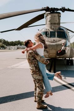 a man and woman standing in front of a helicopter with their arms around each other