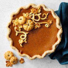 a pumpkin pie with caramel toppings on a white surface next to two pieces of blue cloth