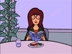 a woman sitting at a table with a plate of food in front of her reading a book