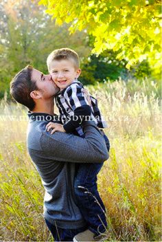 a father kissing his son in the middle of a field with tall grass and trees