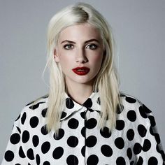 a woman with long blonde hair wearing a polka dot shirt and red skirt, posing for the camera