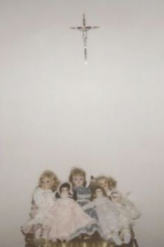 a group of dolls sitting on top of a table under a crucifix