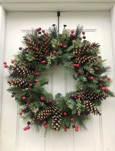 a wreath with pine cones and berries hanging on a door