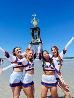 three cheerleaders holding up a trophy on the beach