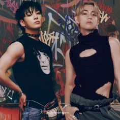 two young men standing next to each other in front of graffiti covered wall with their hands on their hips