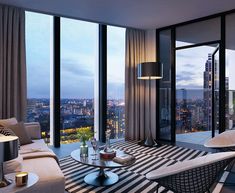 a living room filled with furniture and large windows overlooking the city at night in front of them