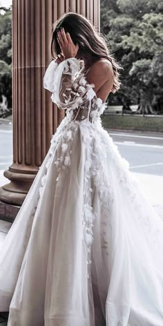 a woman in a white wedding dress standing on the sidewalk with her hands to her face