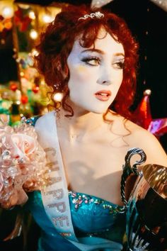 a woman with red hair wearing a tiara and holding a trophy in her hand