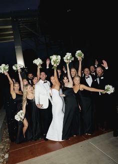 a group of people standing next to each other holding bouquets in the air with their hands up