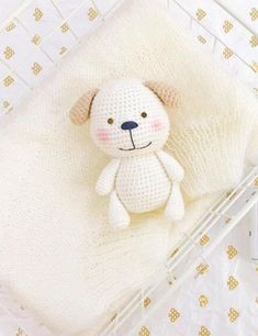 a crocheted white teddy bear laying on top of a blanket in a crib