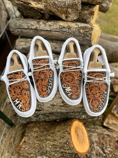 three pairs of white shoes with brown and orange designs on them hanging from a tree log