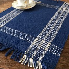 a blue and white plaid table runner on a wooden table with a teacup in the middle