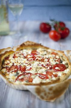 a pizza sitting on top of a wooden table next to some tomatoes and other vegetables