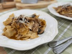 two plates of pasta with mushrooms and cheese on them next to a fork, knife and spoon