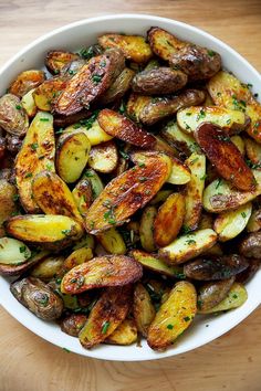 a white bowl filled with cooked potatoes on top of a wooden table