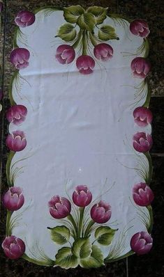 a white table cloth with pink flowers and green leaves on the edges is sitting on a tile floor