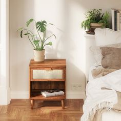 a bedroom with a bed, nightstand and plant on the side table next to it