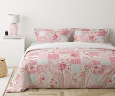 a bed with pink and white quilts on it in a room next to a lamp