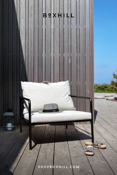 An outdoor lounge chair with white cushion and black frame placed on a wooden deck patio against wooden wall