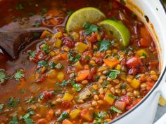 a white pot filled with soup and garnished with cilantro, carrots, beans, and lime