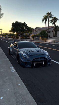 a blue sports car is driving down the street at sunset or dawn in front of some palm trees