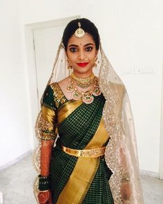 a woman in a green and gold sari with jewelry on her neck, standing next to a white wall