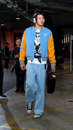 a man with headphones on walking down the street wearing blue sweatpants and a yellow jacket