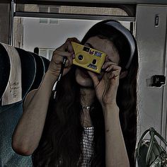 a woman holding a camera up to her face while sitting on a train seat with other people in the background