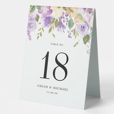 a table number card with purple flowers and greenery is displayed on a white background