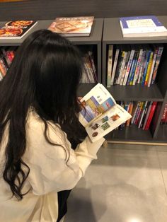 a woman reading a magazine in front of a book shelf with books on the shelves