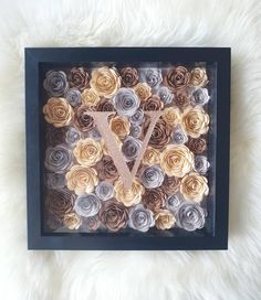 a black frame with some paper flowers and a letter v on the front in it