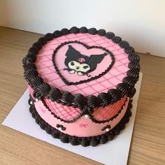 a pink and black cake on top of a wooden table next to a white paper