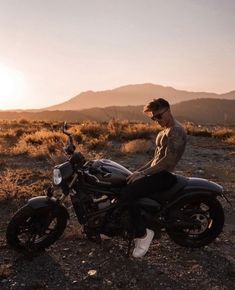 a man is sitting on his motorcycle in the middle of an open field at sunset