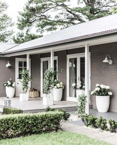 two large white planters sitting on the front porch of a gray house with windows