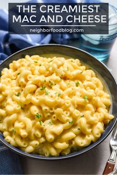 a bowl filled with macaroni and cheese on top of a blue cloth next to silverware